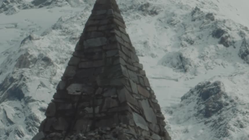 A tall pyramidshaped stone structure stands against a backdrop of snowy mountains