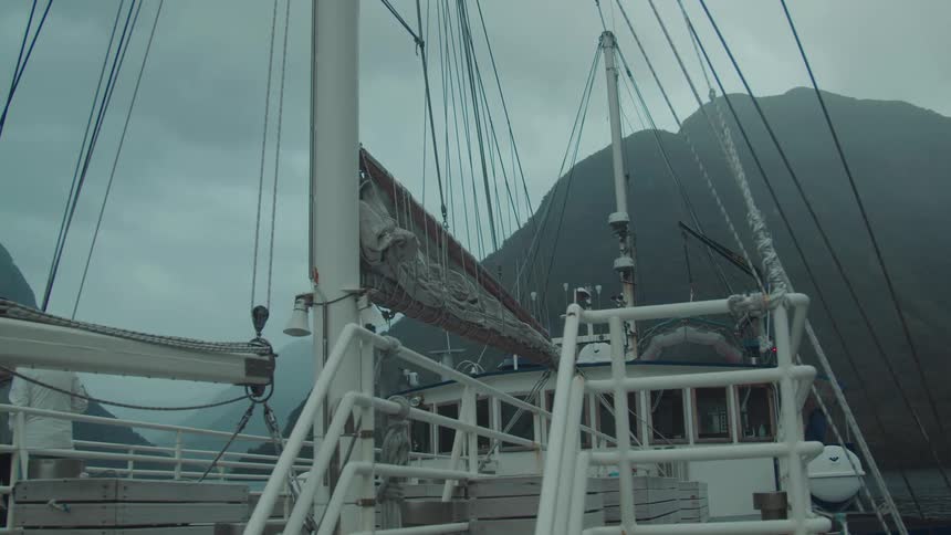 A docked sailboat is framed against misty mountainous terrain under overcast skies