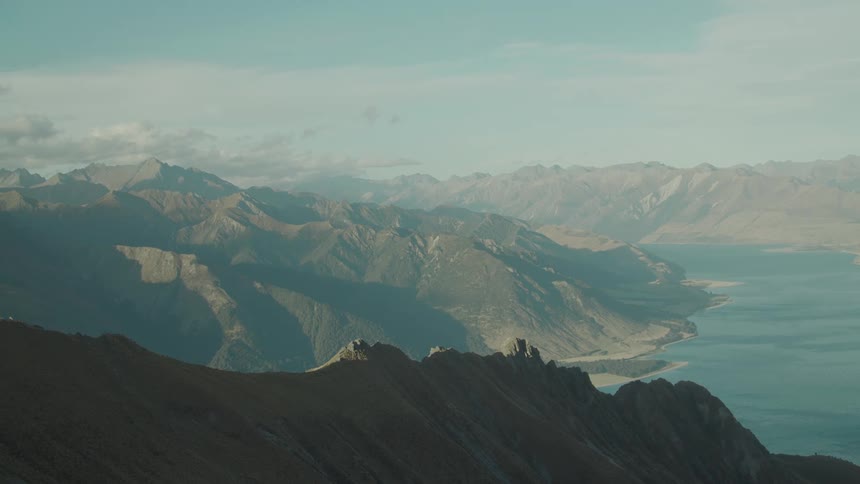 A wide aerial view of a mountain range alongside a large lake under a clear sky