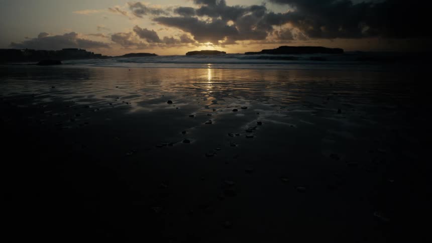 Sunset glows over a calm beach reflecting off wet sand and distant islands