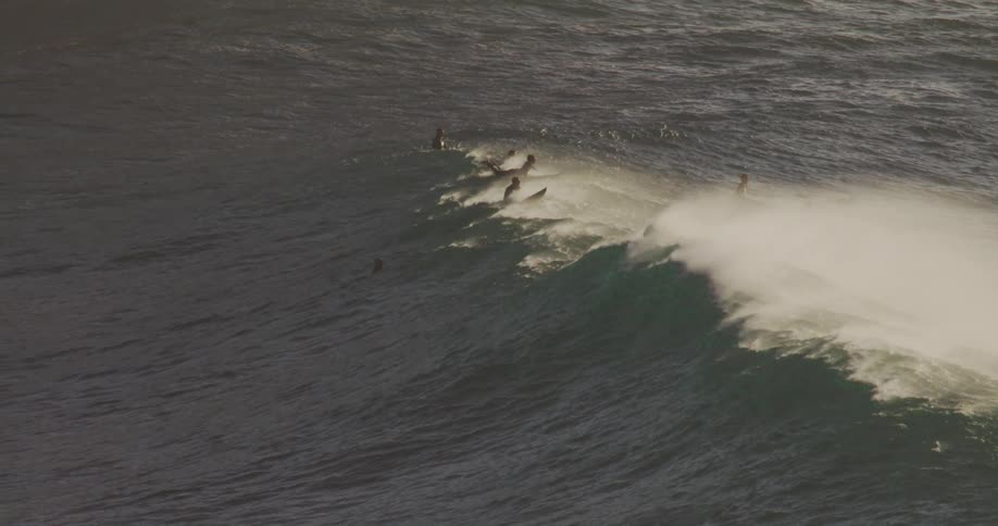 Surfers ride over the top of a wave before it starts to roll
