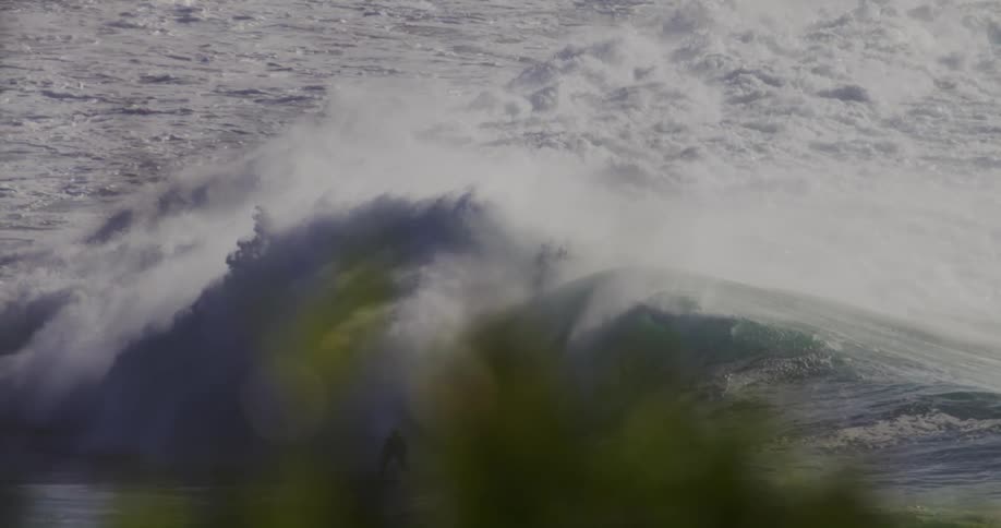 A person surfing on a large powerful wave in the ocean under the bright midday sun