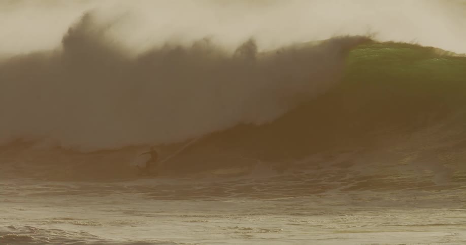 A surfer is riding a large goldenbrown wave silhouetted against its face