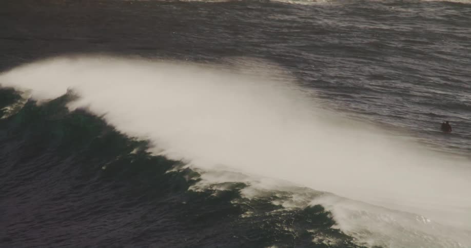 Several surfers are spread across the dark choppy ocean as a white wave breaks under them