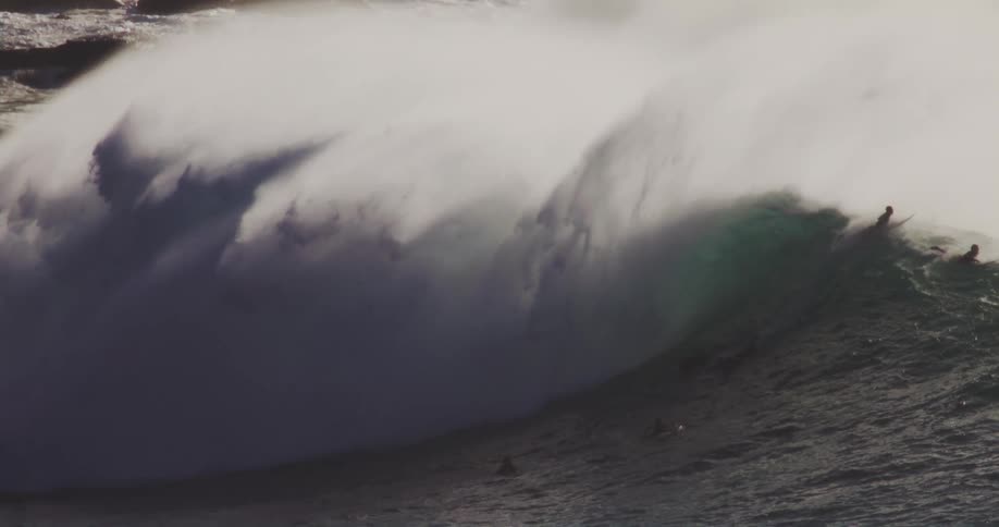 Two men decide not to ride a large wave as it breaks near a rocky beach