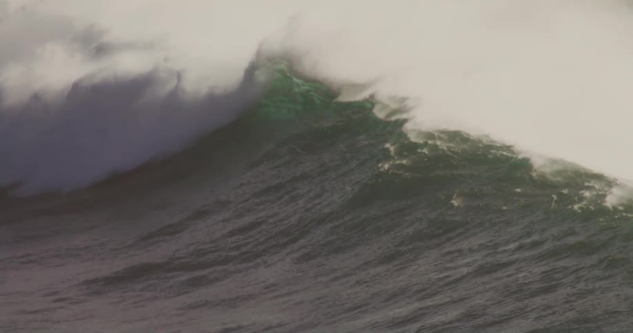 A person riding a surfboard over a powerful wave forming in the ocean at midday