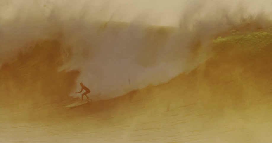 A surfer riding the goldenbrown curl of a large breaking ocean wave enveloped in a mist of spray