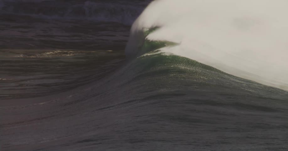 A big wave and a person in the sea outside the wave sitting on a surfboard