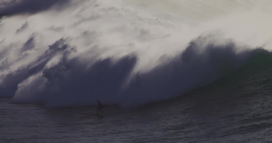 A surfer rides a wave that towers over him