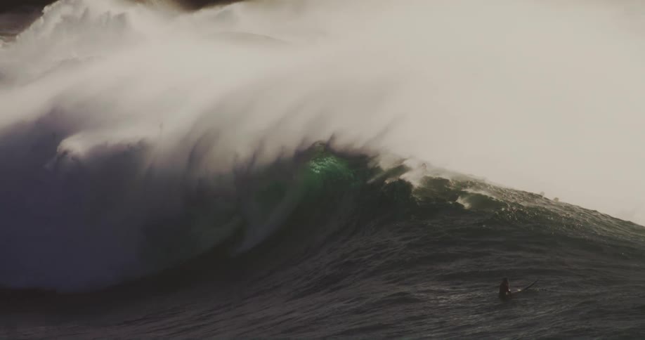 A big wave and several people in the sea sitting on their surfboards