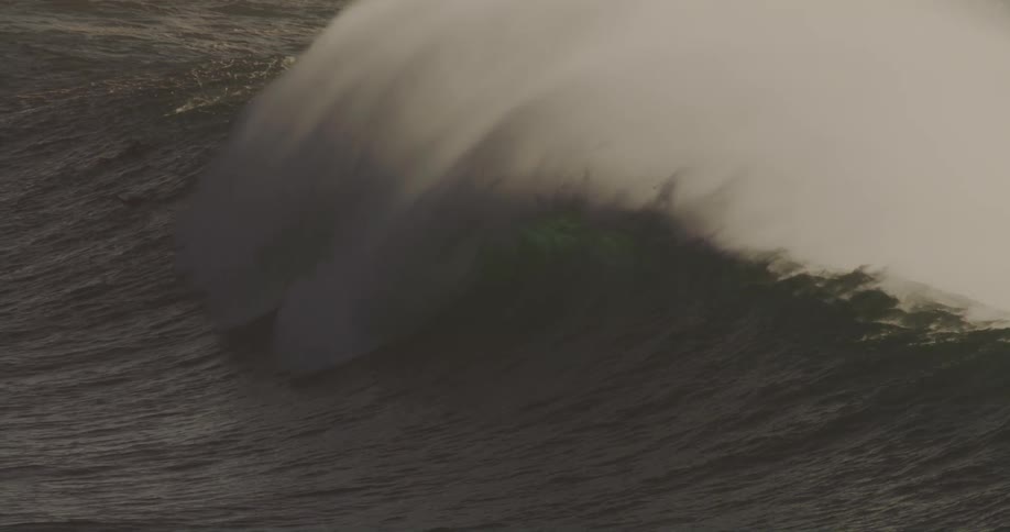 A large ocean wave crests and breaks generating a massive plume of white spray across its surface