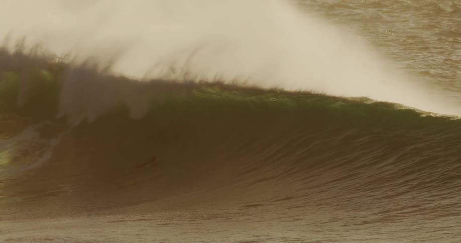 A surfer paddles toward a massive wave about to break in the ocean