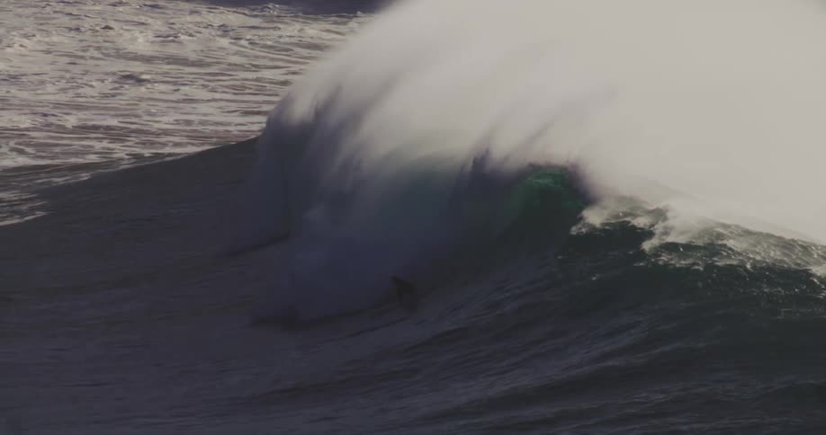 A surfer rides a large wave barely staying ahead of it