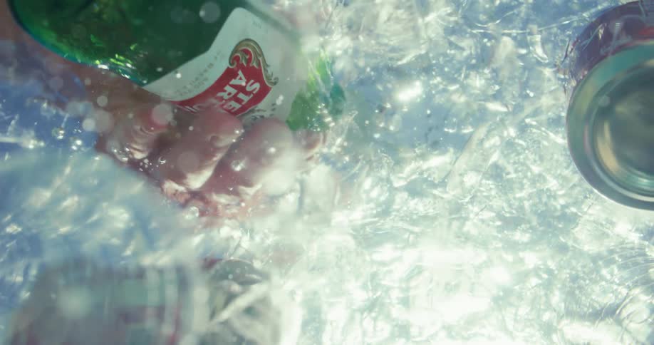 Person grabs a bottle from among the beverages floating in an ice chest during the daytime