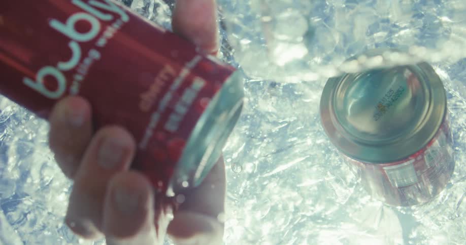 A hand reaches down in the ice to grab a can of seltzer