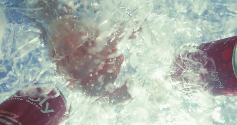 A hand reaches down into the ice cans of soda floating