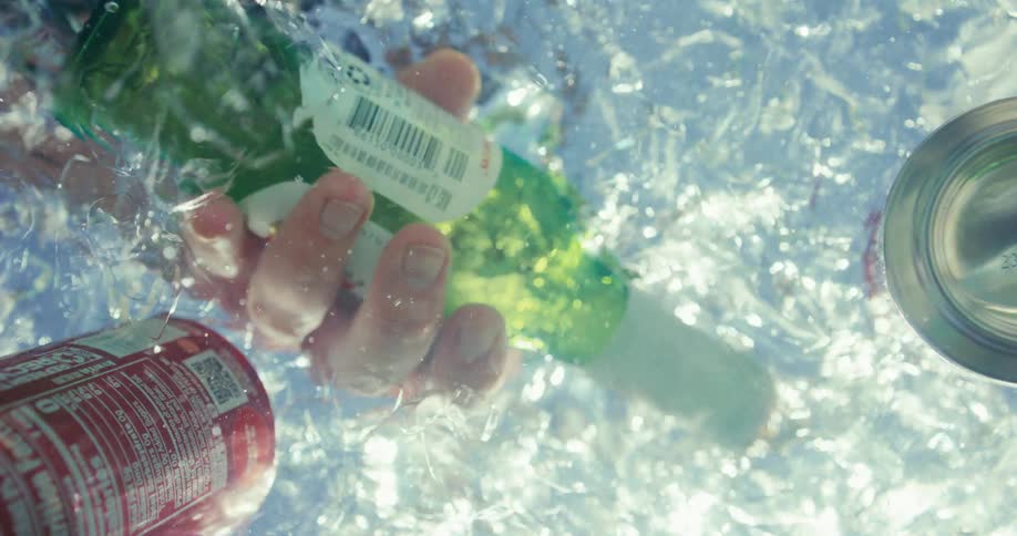 Hand pulls a bottled beverage from an ice chest during the daytime
