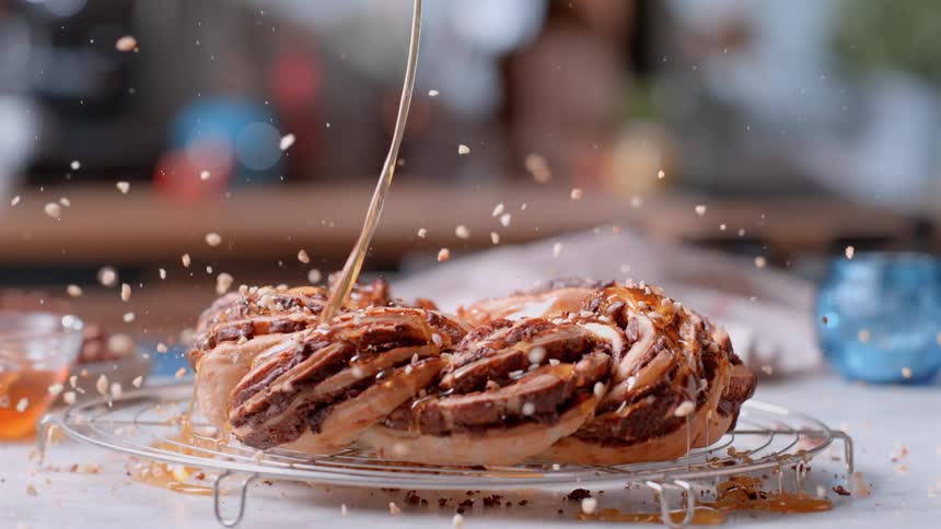 Flowing syrup and a sprinkle of nuts cover a dessert pastry sitting on a rack