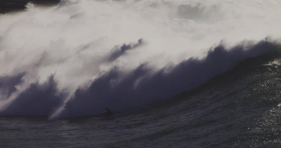 One surfer rides a breaking wave while other surfers remain on their bellies on their boards