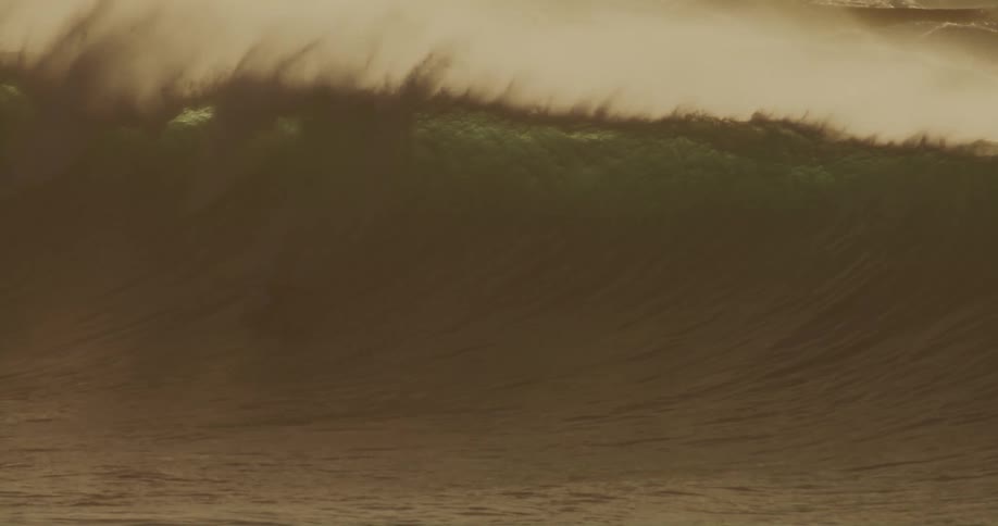 Surfer rides a large breaking wave as it sprays water into the air