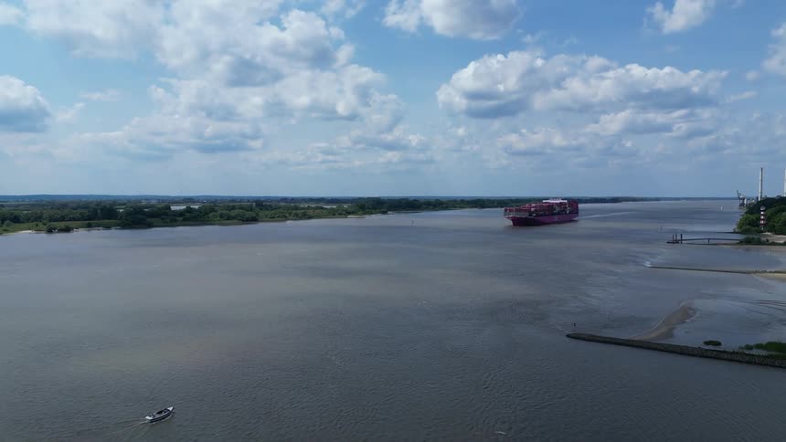 Container ship moves along the river leaving a wake on a cloudy day