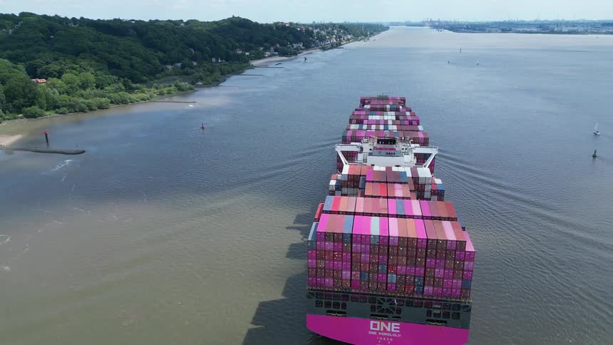A cargo ship carrying many shipping containers sailed in the ocean near the shore at midday