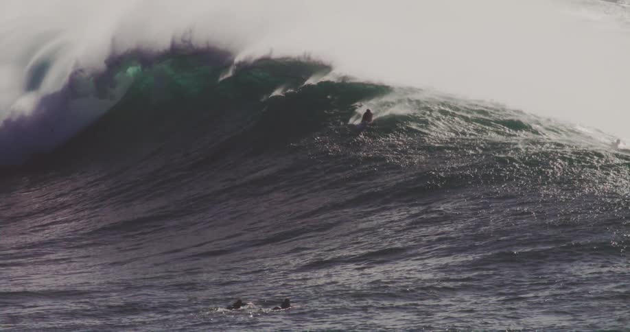 Surfers lie on their surfboards while the wave swells and breaks