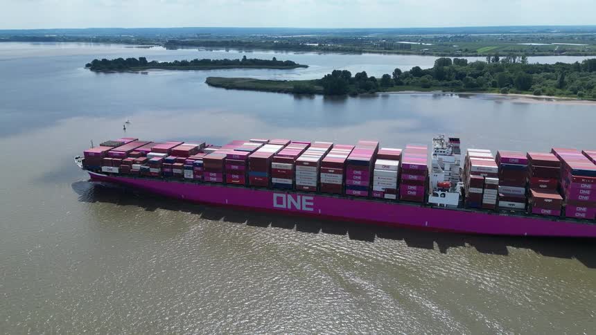 Loaded container ship travels through the water near a forested shore