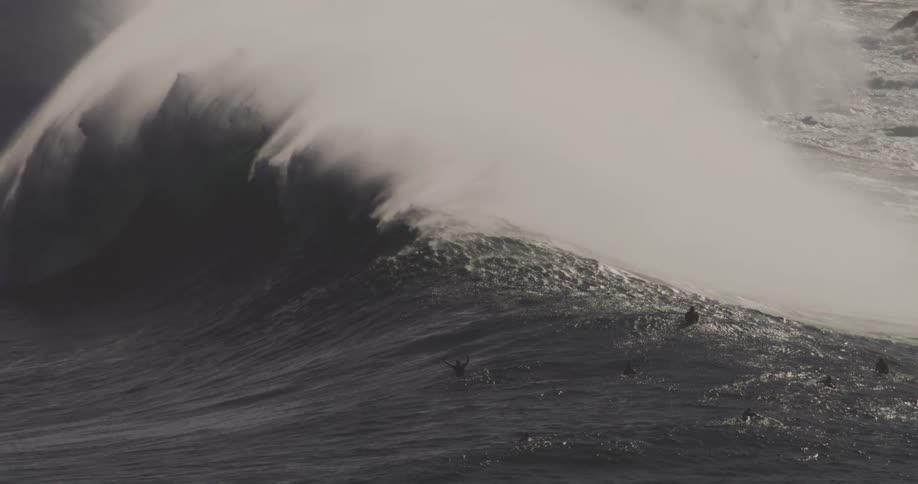 Surfers float in the water as a large wave crashes on the rocks