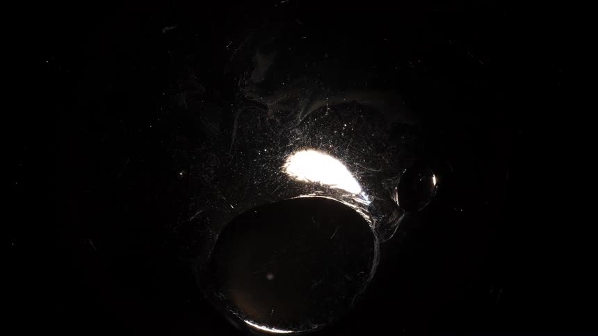 A bright reflective bubble hovers over a light on a dark textured surface