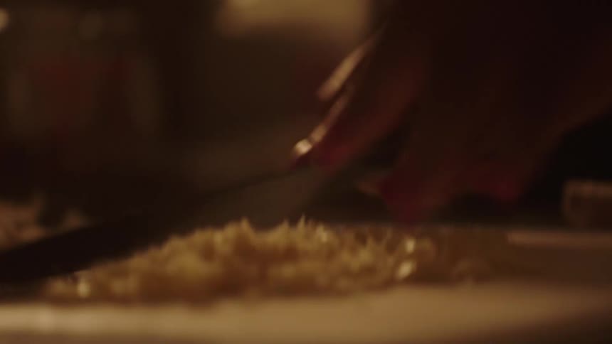 Pair of hands with a knife cutting food on top of a wooden board