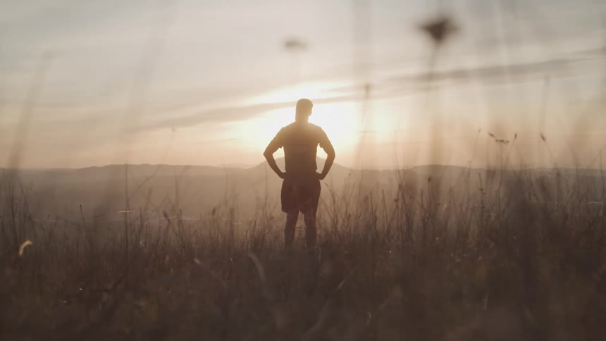 The man is watching the sun rise from the tall grass
