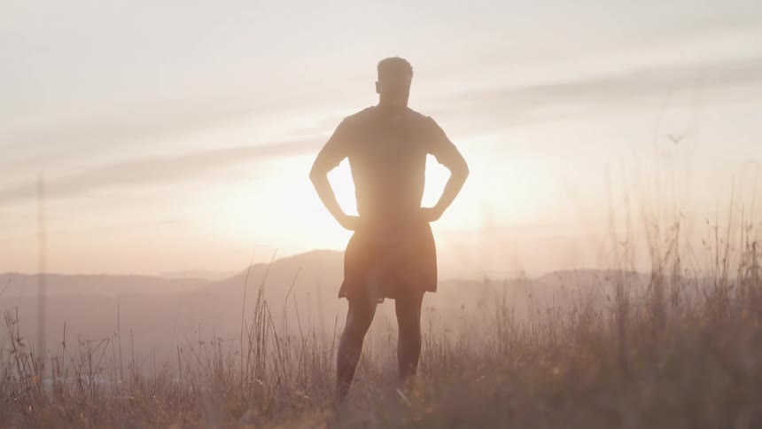 A man stands silhouetted against the setting sun