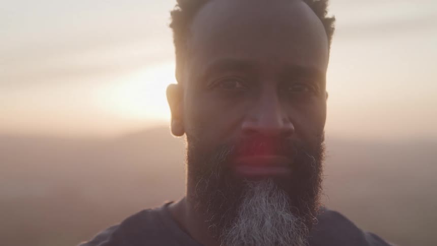 A bearded older man standing under the setting sun
