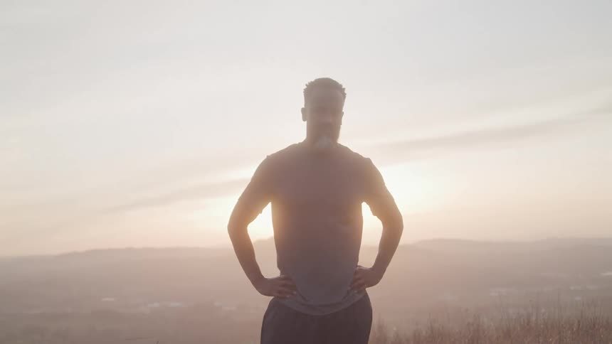 Silhouette of a man with hands on hips in an outdoor setting at dawn