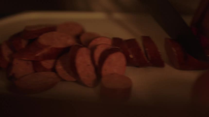 A person slicing a sausage on a cutting board with a knife