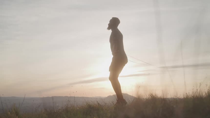 A man skipping rope on a grassy field as the sun sets casting a warm golden glow over the landscape