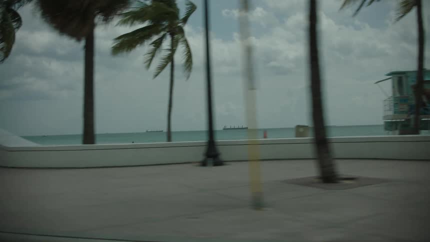 A coastal road with people walking along it at midday with a clear view of the ocean in the background