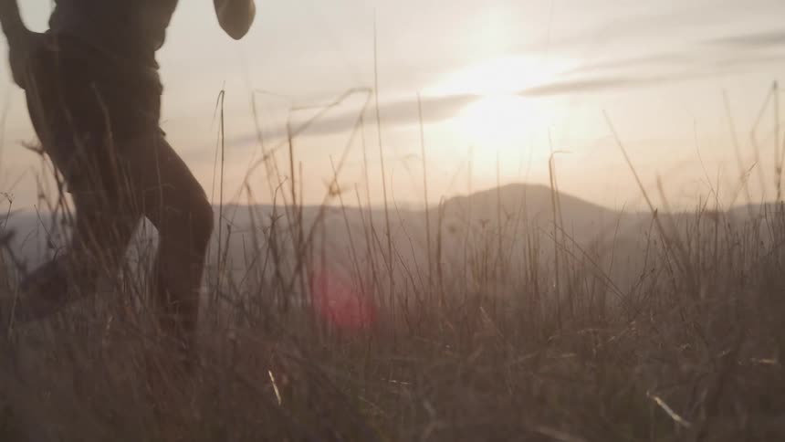 A man running up a grassy hillside at sunset with golden light casting long shadows across the landscape