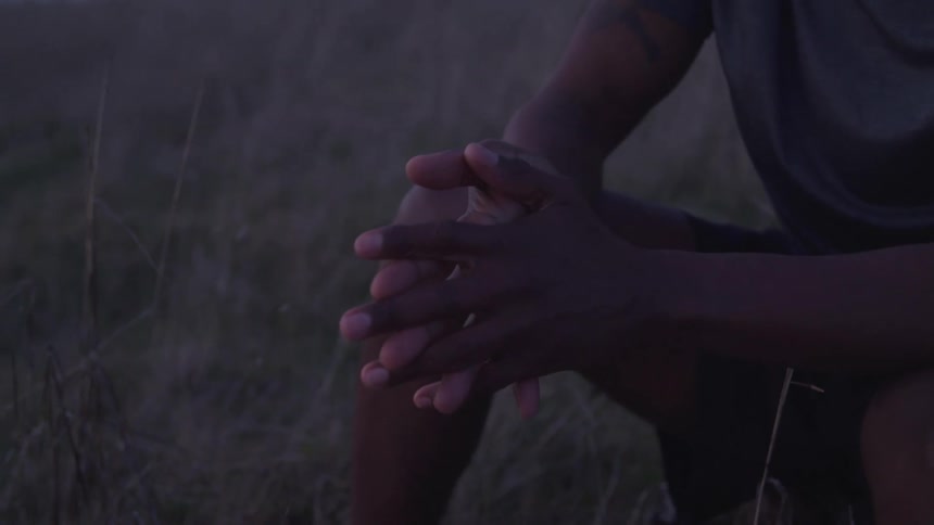 A man is sitting in the grass and rubbing his hands together