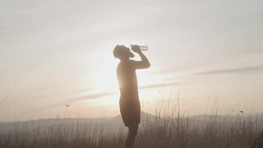 A man standing under sunlight drinking water from a bottle