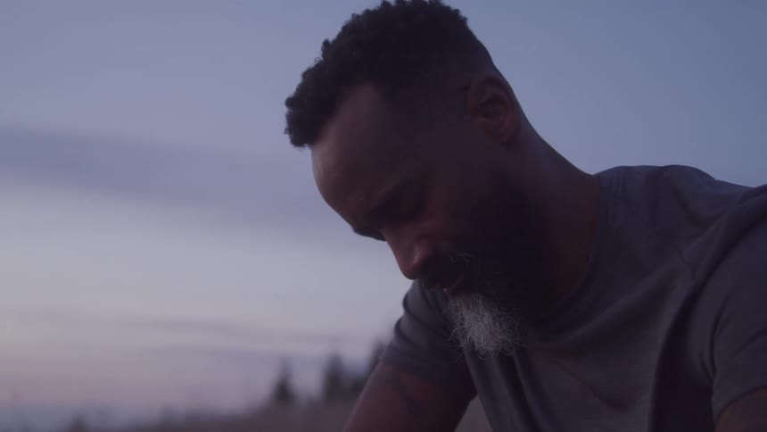 Bearded man looking down while standing in an outdoor setting