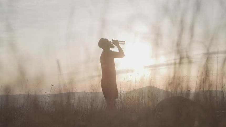 Silhouette of a man outdoors drinking from a bottle