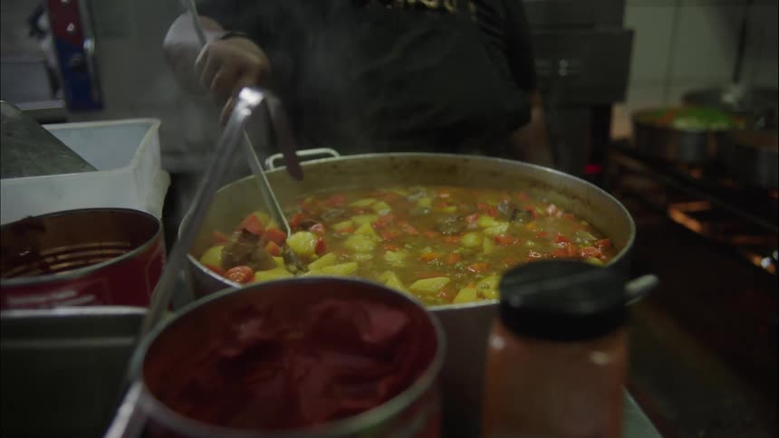 Person with a ladle cooking meat and vegetables in a large pot