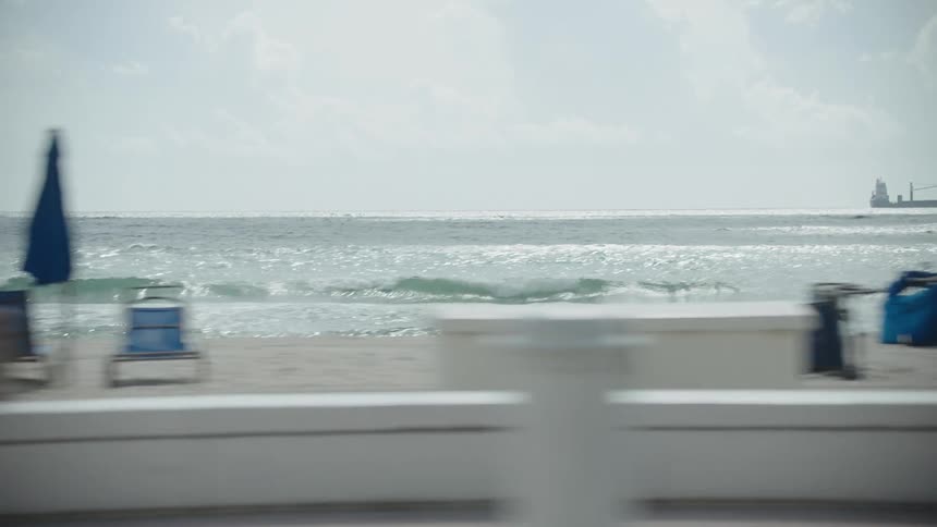 Blurred beach view with empty lounge chairs and a palm tree in motion near the ocean