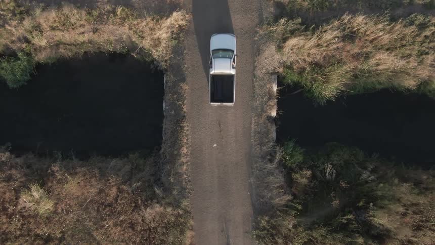 Pickup truck crosses a small bridge connecting fields during the daytime