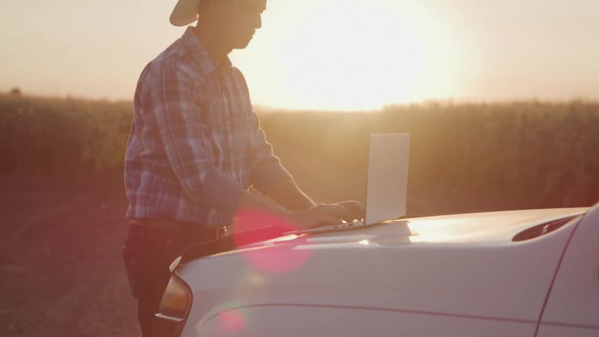 A man typing on a laptop placed on a car with intense sunlight in the background