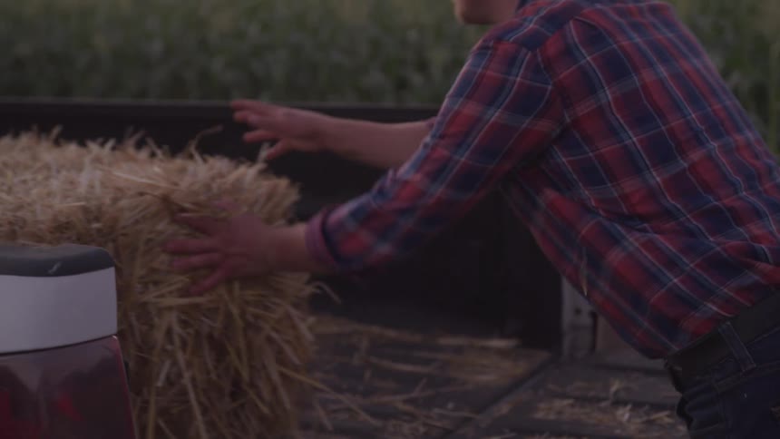 A farmer pushes a large bale of hay into a truck bed