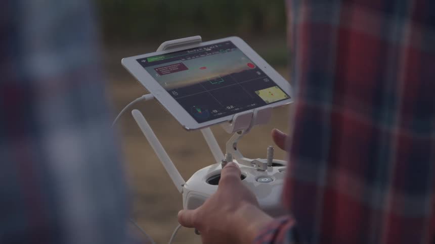 Close up of a person outdoors operating a drone controller connected to a tablet device