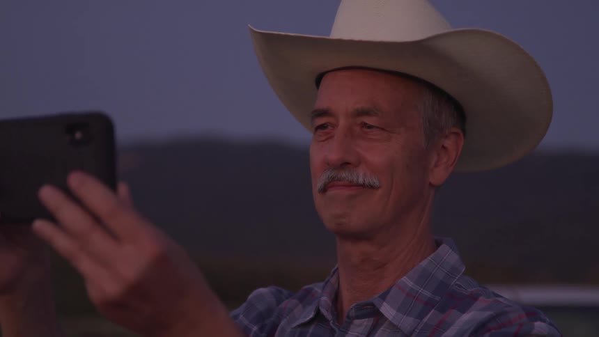 A man wearing a cowboy hat holds a smartphone horizontally in front of him